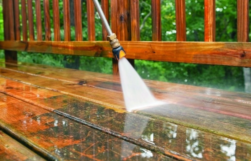 Power washing a wooden deck in Woodbridge, VA, as a spray wand rinses the wet boards.